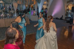 Wedding party members dancing together during a reception on a wooden dance floor.
