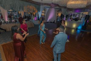 Wedding guests dancing and enjoying themselves at an indoor reception venue with purple lighting.