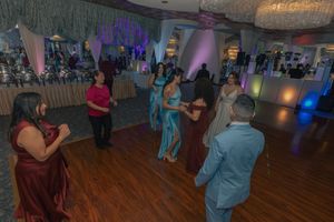 Wedding guests dancing at an indoor reception with decorative lighting and white drapes.