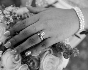 Close-up of hands with wedding rings resting on white roses in black and white.