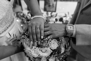 Wedding rings and hands photographed with floral arrangements in monochrome style.