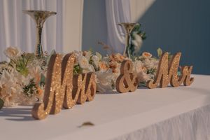 Gold decorative wedding signage displayed on white table with floral accents.