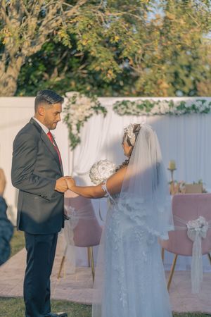 Wedding couple poses outdoors with white chairs and trees in the background.