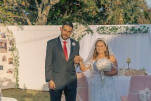 Outdoor wedding scene with white backdrop and natural foliage overhead.