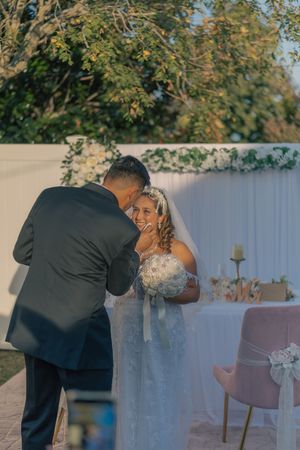 Candid wedding moment captured in an outdoor garden setting with decorative backdrop.
