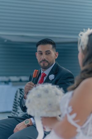 A groom in a dark suit and red tie smiles during a wedding ceremony.
