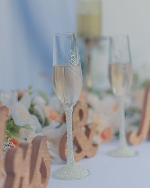 Crystal champagne glasses lined up on a table with soft floral decorations.
