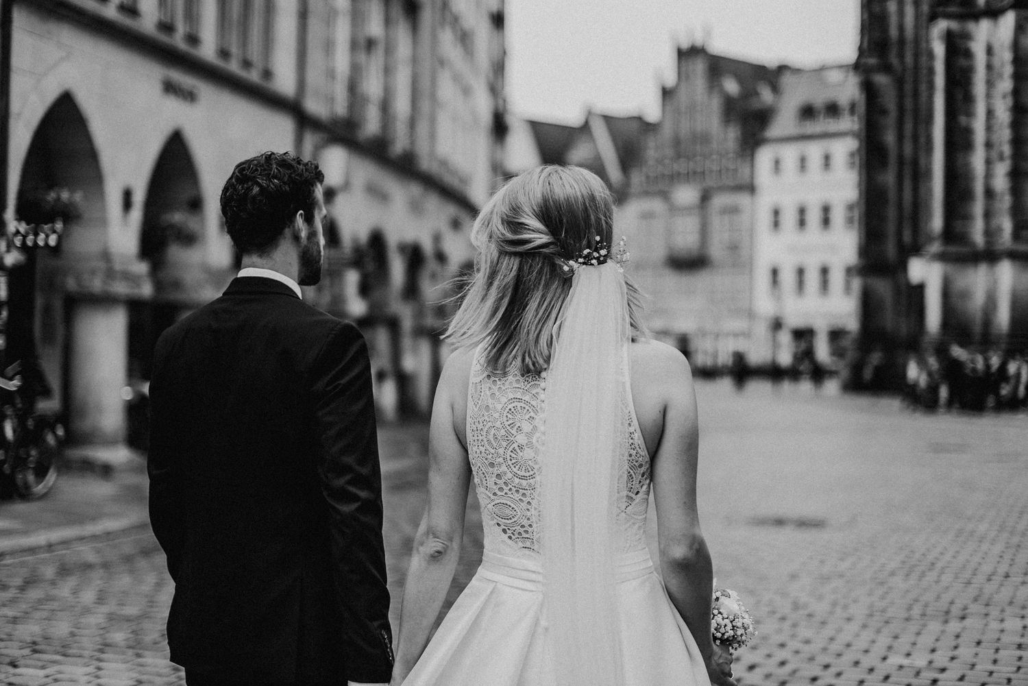 Ein Brautpaar schlendert über den Prinzipalmarkt in Münster, Perspektive von hinten. Schwarz-Weiss Hochzeitsfoto.
