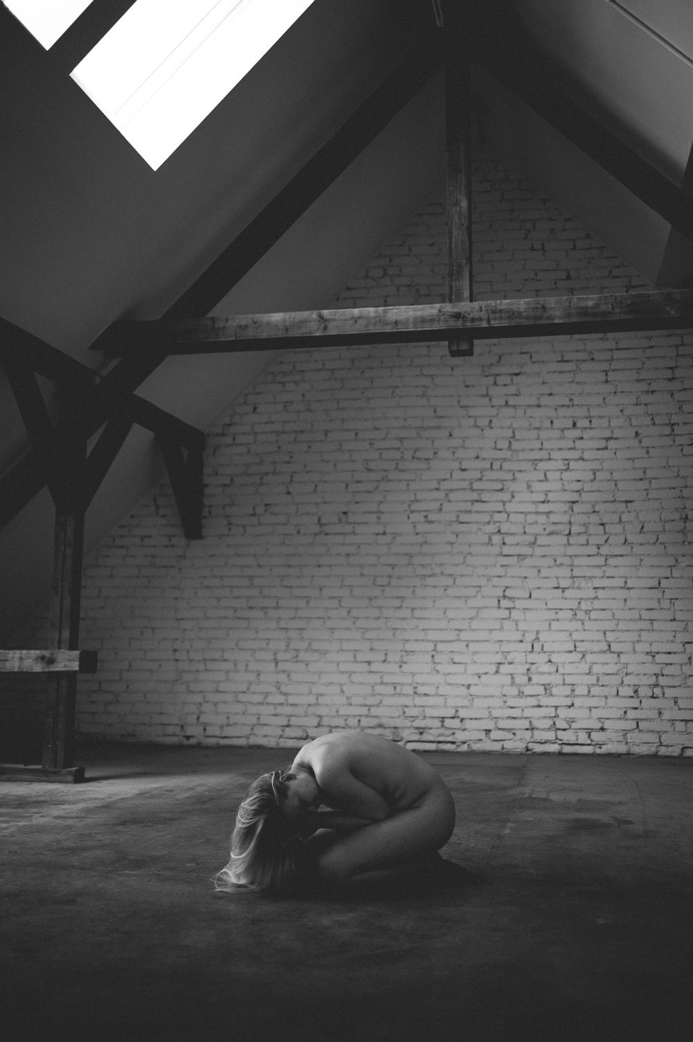 A black and white photo series showing a person lying on the floor of an empty brick attic space in different positions.