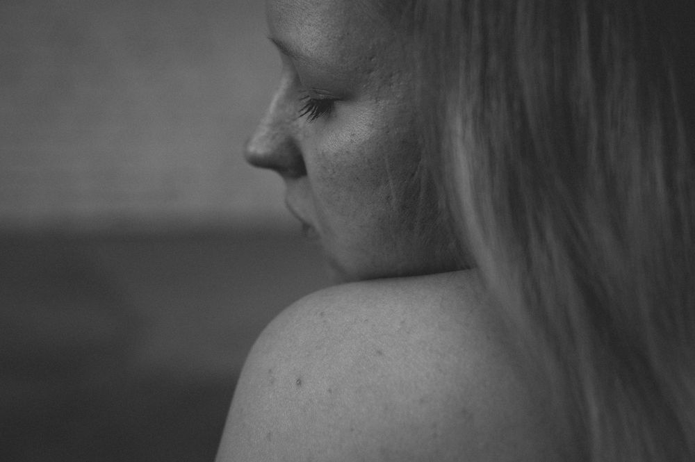 Black and white close-up profile view of someone with light hair, showing bare shoulder and soft facial features.