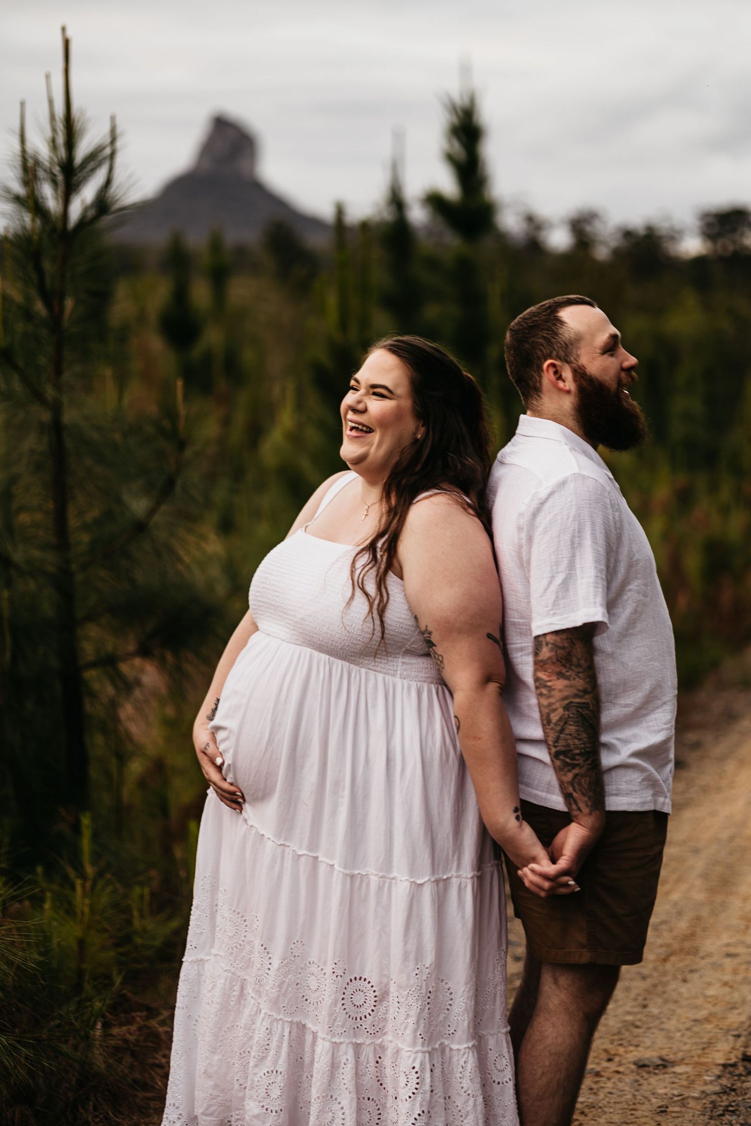 An expecting mother holding her husbands hands in the glasshouse mountains for their maternity photoshoot