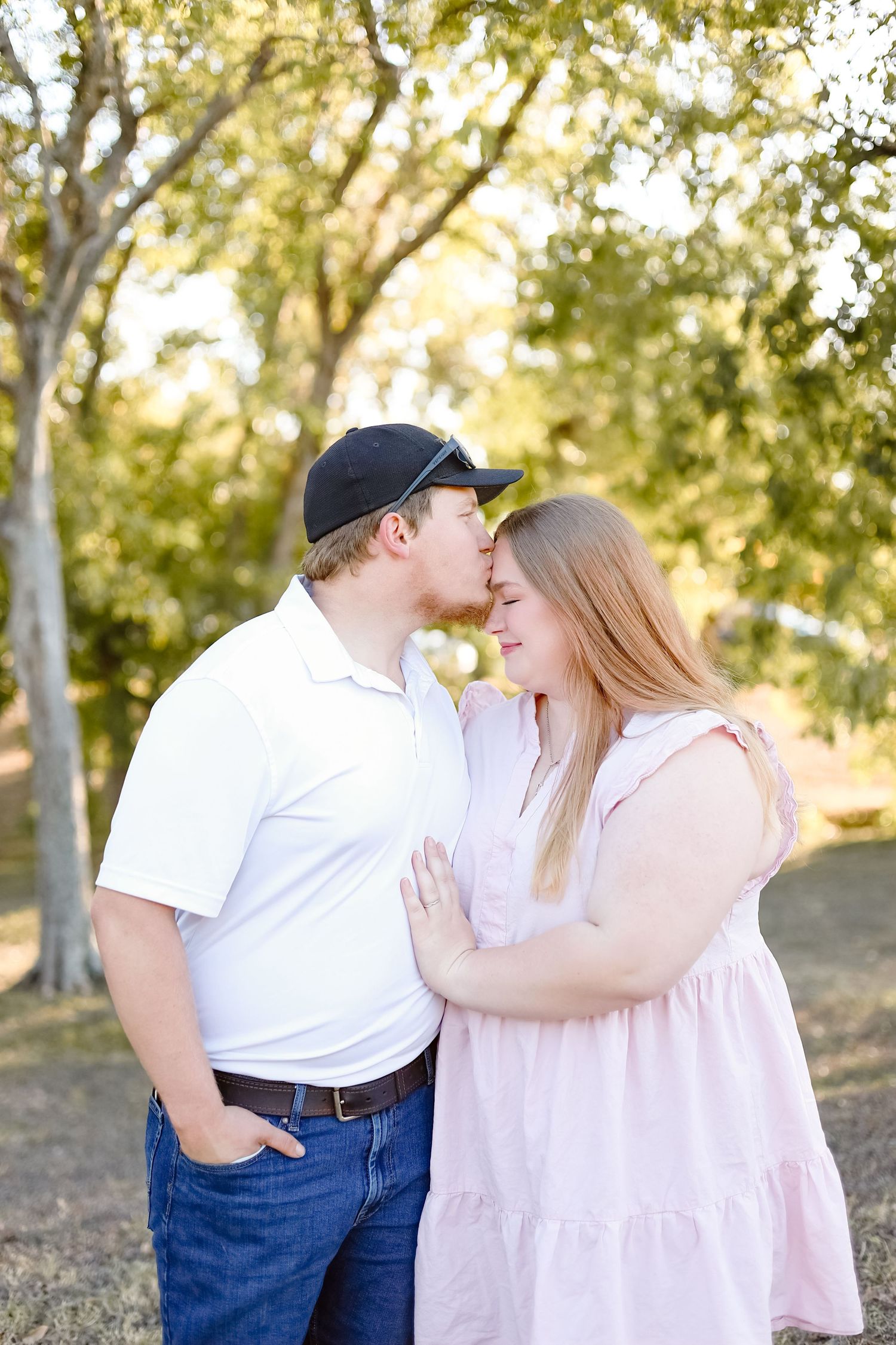 A couple shares a romantic moment outdoors against a backdrop of sunlit trees in a natural setting.