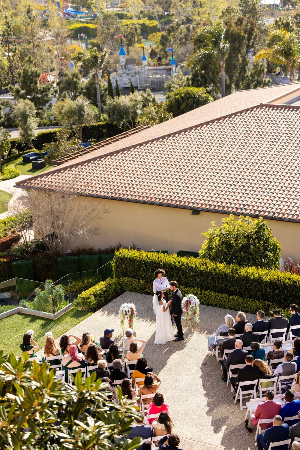 Aerial view of an outdoor wedding ceremony at a Mediterranean-style venue with tiled roof and garden landscaping.