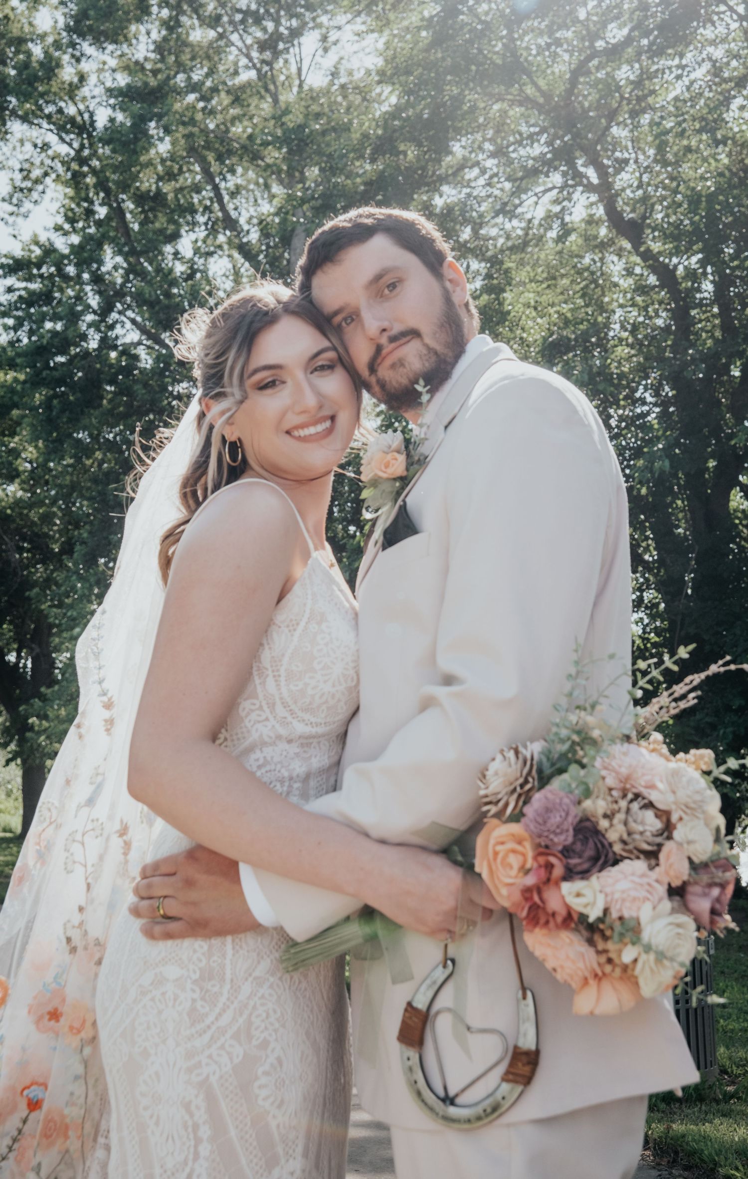Romantic outdoor wedding portrait of a couple in white attire holding a colorful bouquet.