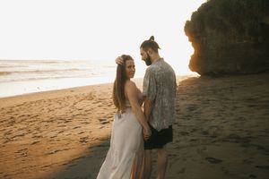 Couple walking hand in hand on a sandy beach during golden hour with cliffs and ocean waves in view.