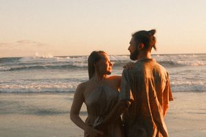A couple walks together along a scenic beach at sunset with waves crashing in the background.