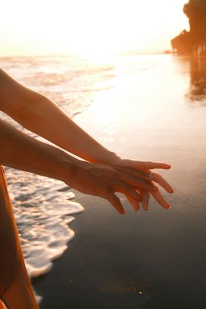 Silhouetted hand reaching out towards a golden sunset over the ocean waves.