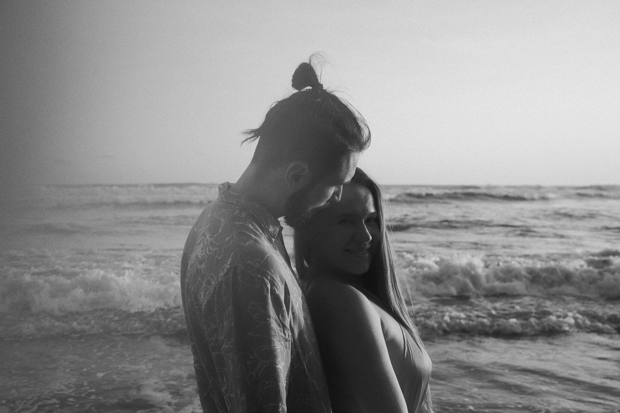 A silhouetted couple embraces on a beach at sunset in black and white.