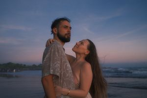 Romantic couple embraces on a beach at sunset with waves crashing behind them on the shoreline.