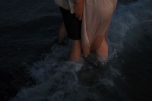 Person walking barefoot in shallow ocean water at sunset creating ripples and reflections in the sand.