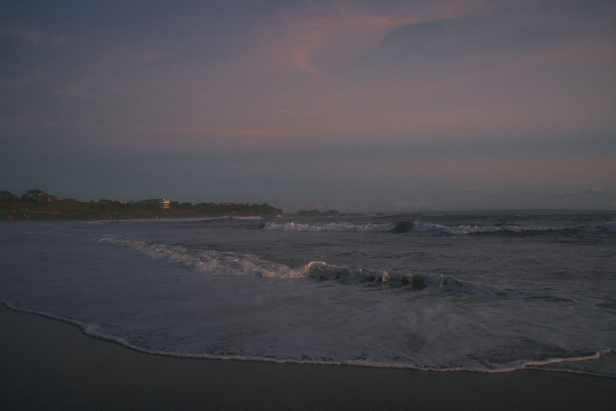 Panoramic view of a misty beach at dusk with gentle waves rolling onto the sandy shore.