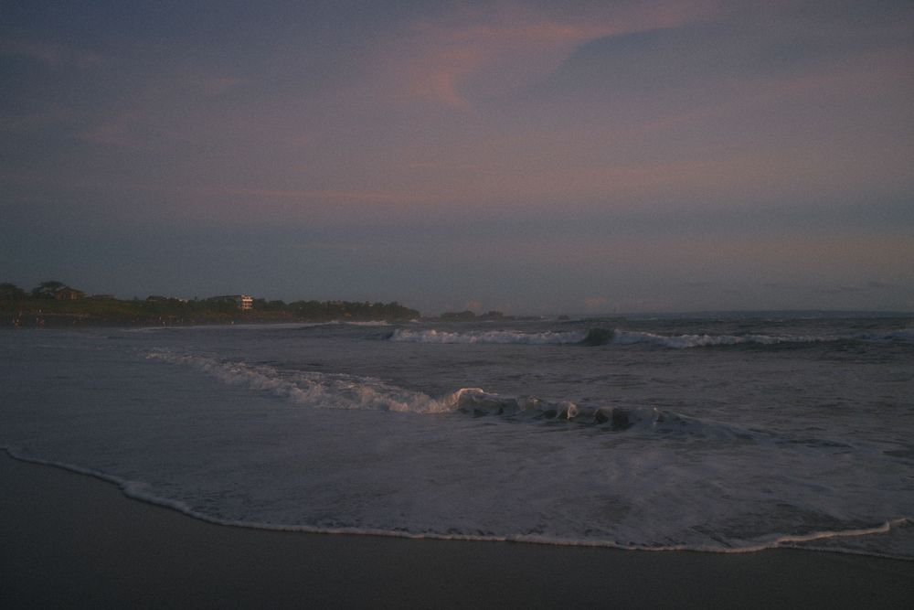 Panoramic view of a misty beach at dusk with gentle waves rolling onto the sandy shore.
