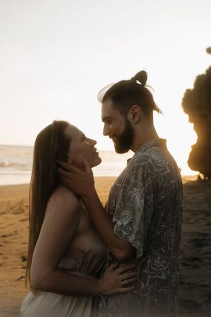 Romantic couple embraces on a beach at sunset with golden light filtering through their silhouettes.