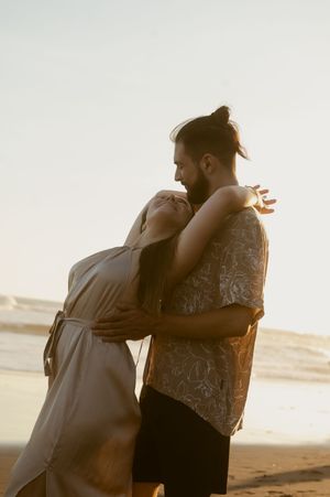 Romantic couple embraces on a beach at sunset creating silhouettes against the golden sky.