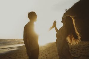 Silhouetted figures walk along a beach at sunset with golden sunlight streaming through their outlines.