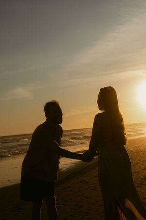 Two silhouettes share a tender moment on a beach at sunset as waves roll in along the shoreline.