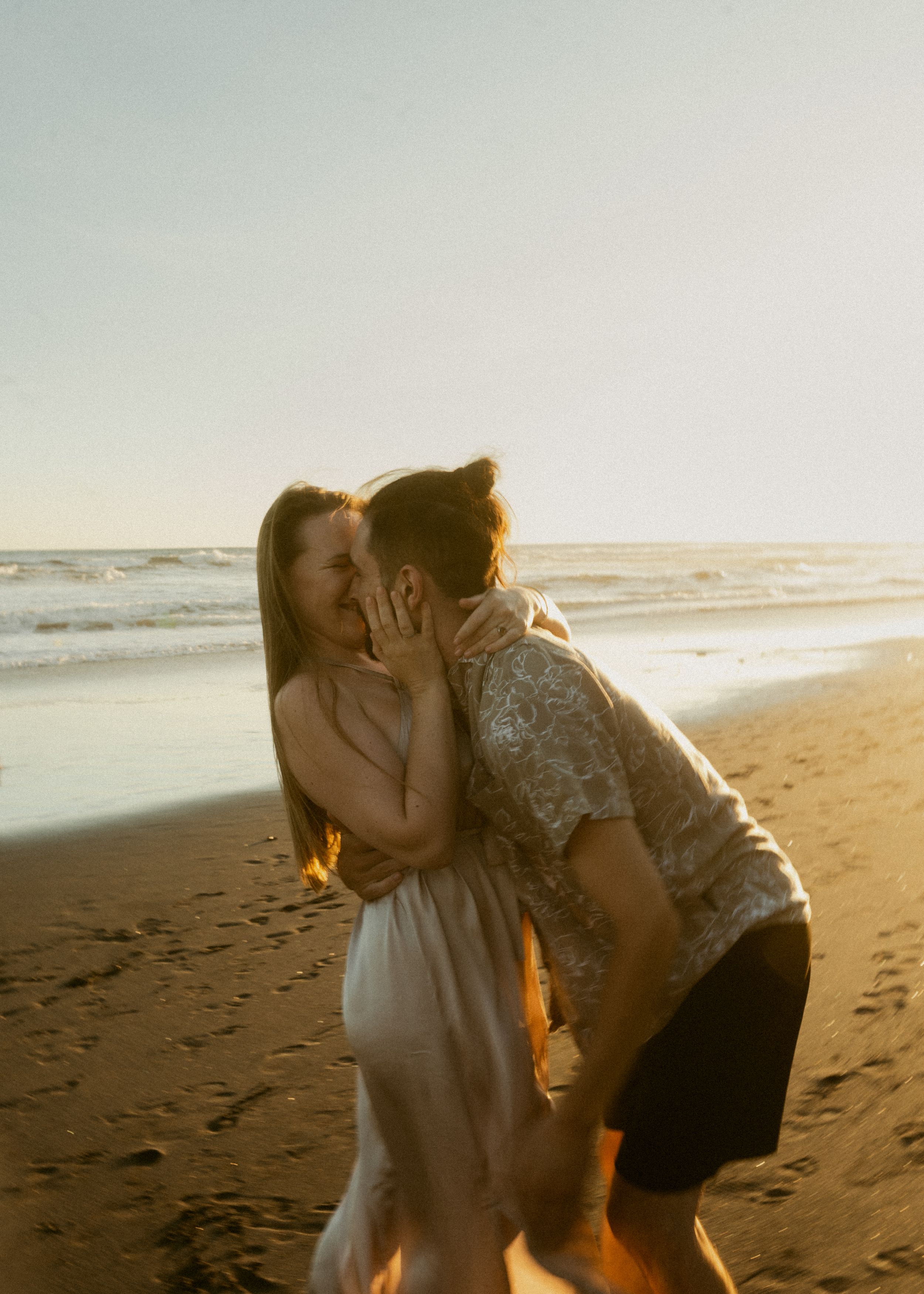 A romantic couple shares an intimate moment together on a sandy beach at sunset.