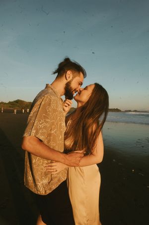 A tender moment between a couple on the beach during sunset, with soft golden light illuminating the scene.