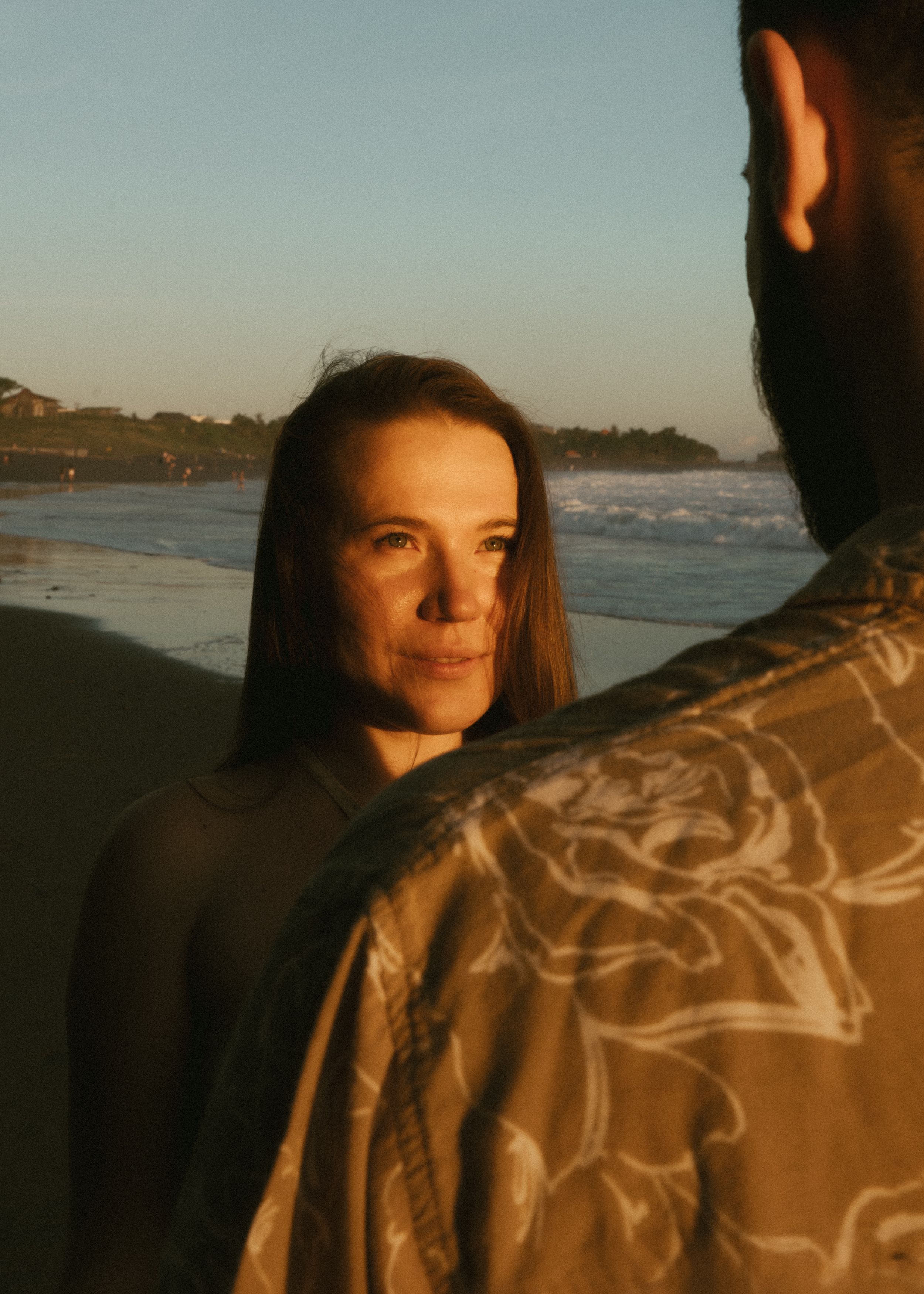 A couple shares an intimate moment on a beach at dusk with mountains visible in the background.