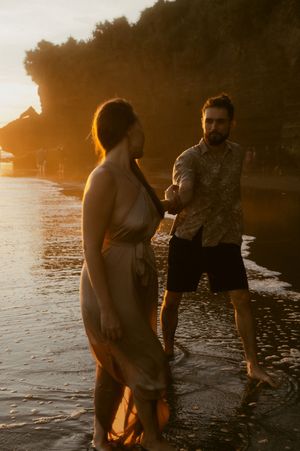 A couple shares an intimate moment on a beach at sunset with golden light reflecting off the water.