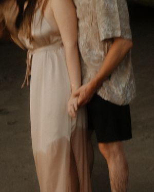 A couple in casual attire stands close together in an intimate pose against a dark background.