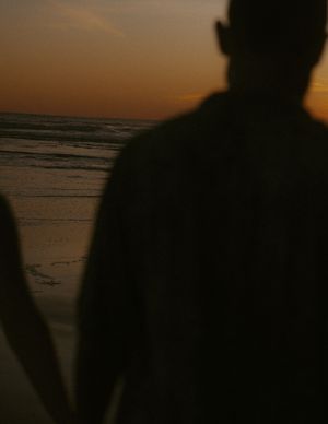 Dark silhouettes of figures on a beach at sunset with an orange glowing sky.