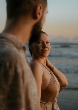 A couple shares an intimate moment on a beach at golden hour with the ocean in the background.