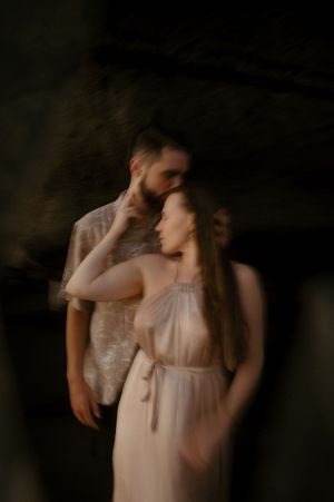 Artistic blurred portrait of a couple in romantic embrace wearing light colored clothing against dark background.
