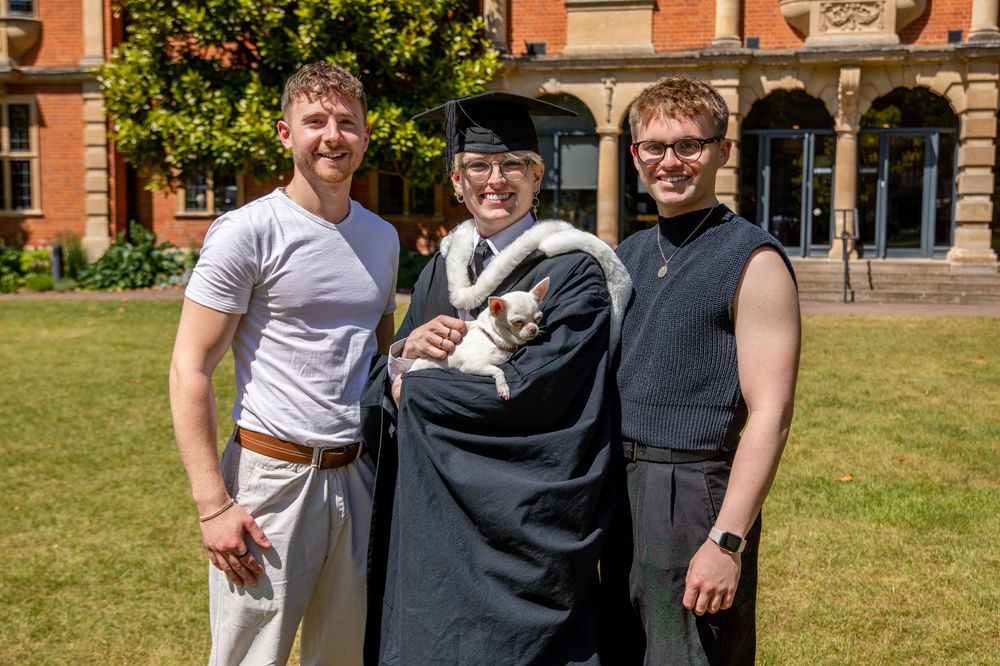 A graduation photo session in front of a historic brick building with green lawn and trees.