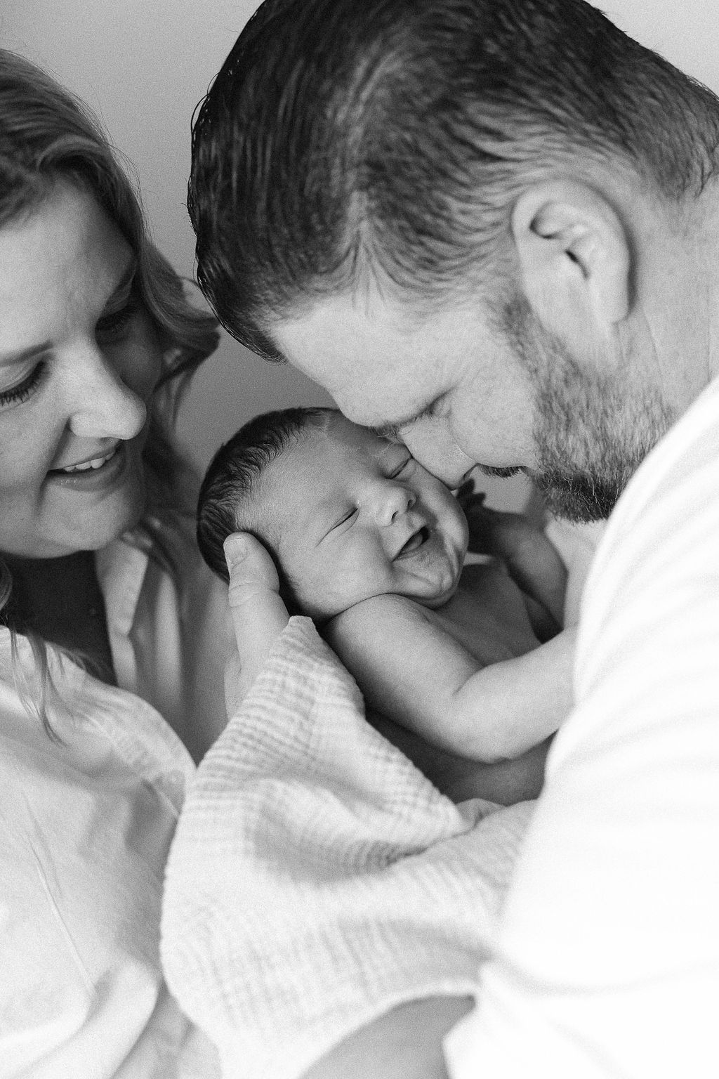 Black and white photograph montage showing tender moments between a parent and newborn baby wrapped in white.