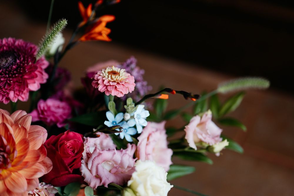 A close-up of a colorful mixed flower arrangement with pink, purple, and coral blooms against a dark background.
