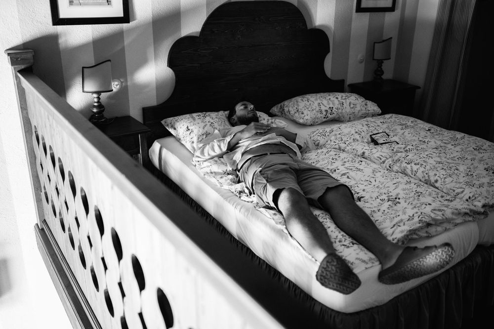 A person lies face down on a bed with a decorative headboard in a black and white photograph.