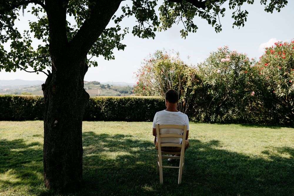 Person sitting alone on a wooden chair in a serene garden setting with mountain views in the background.