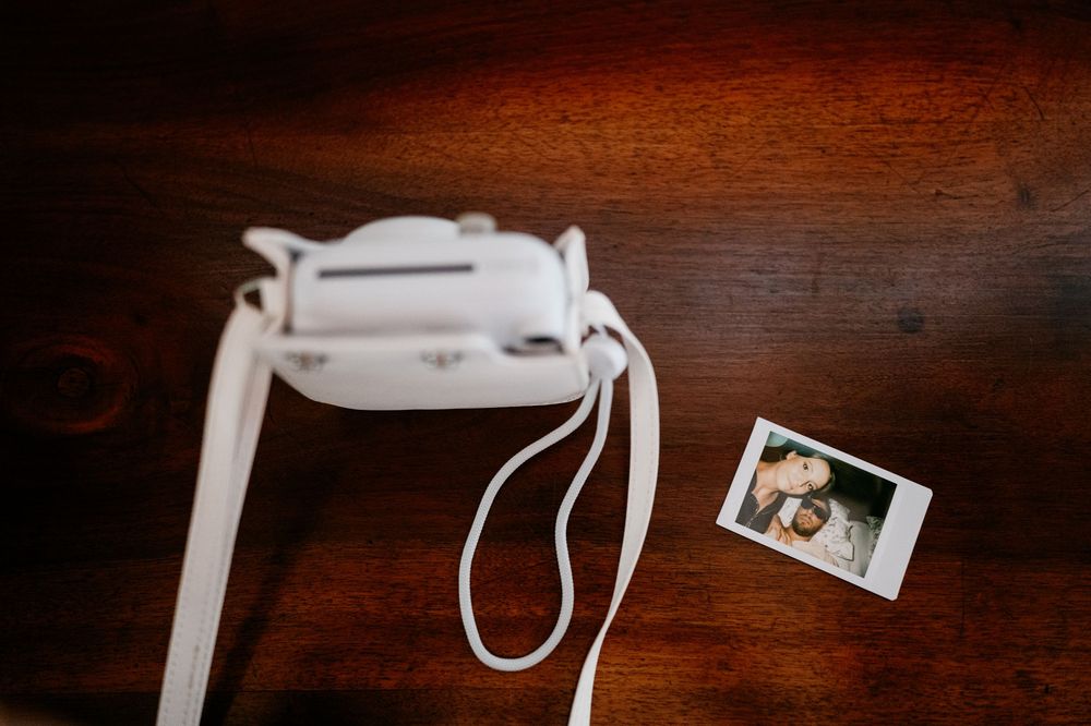 A white Fujifilm Instax camera and a small instant photo on a dark wooden surface.