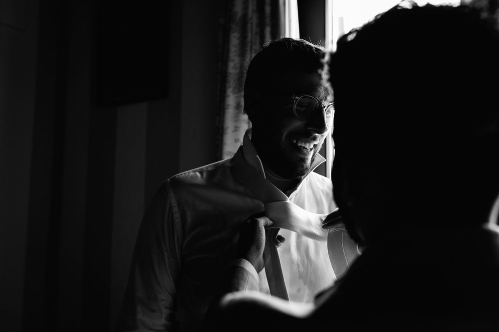 Getting ready scene with someone adjusting white dress shirt and tie in dramatic black and white lighting.