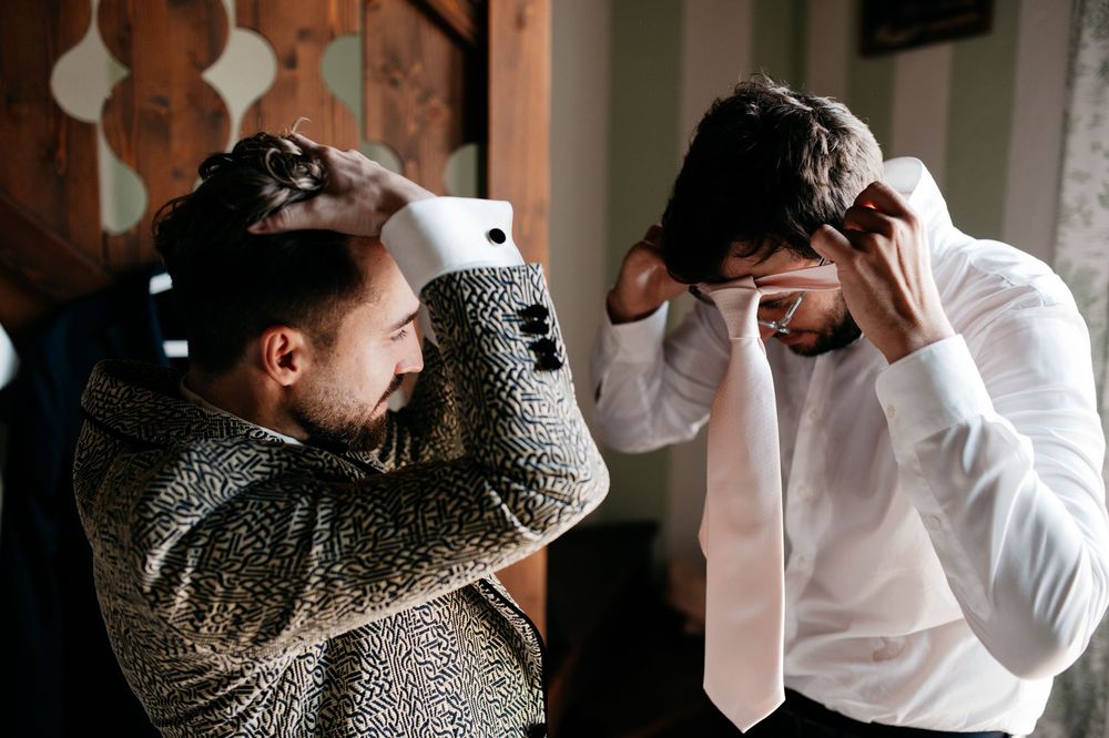 Two people adjusting their ties while getting ready in formal attire.