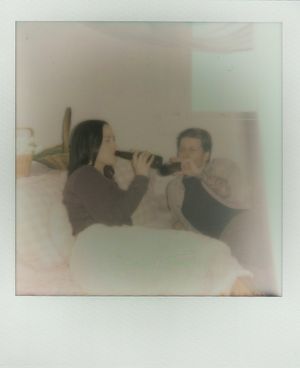 Two people taking selfie photos together using vintage-style polaroid cameras in a dreamy soft-focus setting.