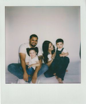 Family of four sitting together for a vintage-style polaroid photo in casual attire against light background.