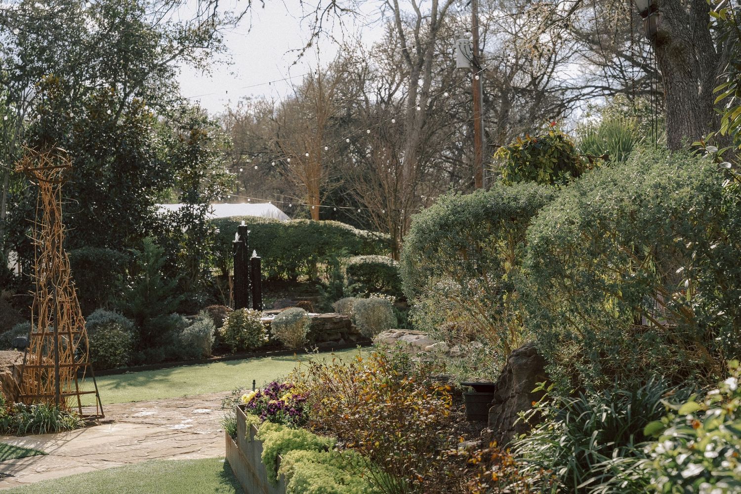 A serene garden path winds through lush greenery with patio umbrellas visible in the distance.