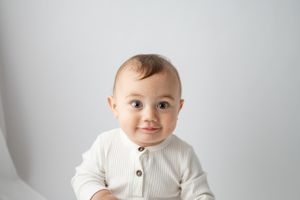 Baby wearing white ribbed sweater poses against plain gray background.